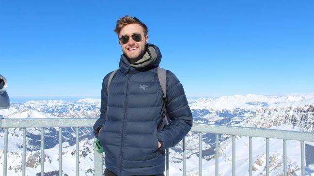 student smiling, outside with Swiss Alps snow mountains in background