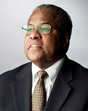 headshot of Prof Houston Baker, an older black man wearing a dark suit, gold tie, and glasses 