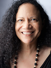Headshot of Alice Randall, a middle aged black woman with loose shoulder length black hair. She is wearing a black blouse and necklace, and has her hands on her hips.