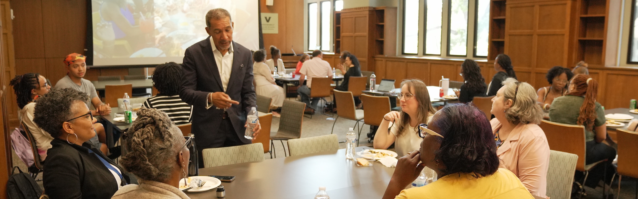 man standing talking to group of people sitting at a table