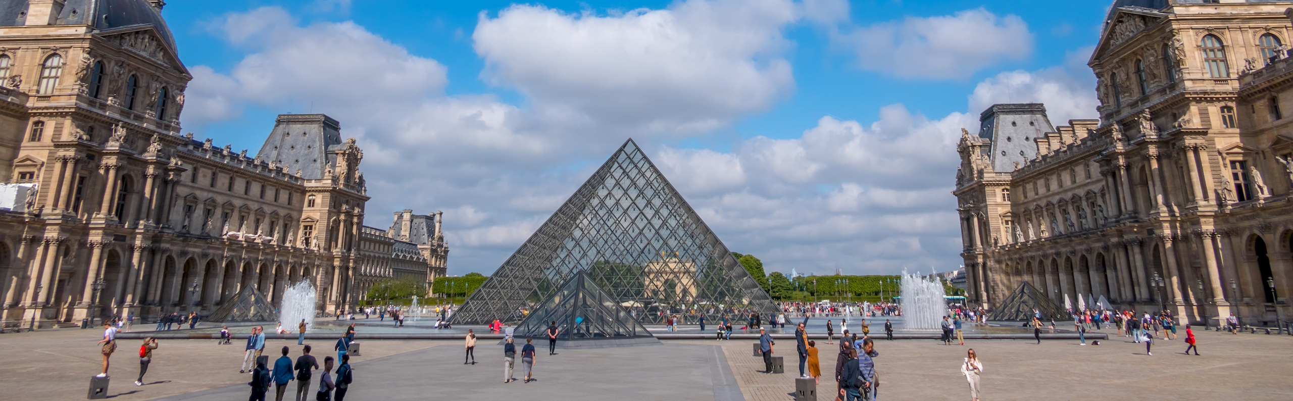 France. Summer sunny weather in Paris. The famous courtyard of the Louvre Museum and the glass pyramids. Many tourists. Clouds