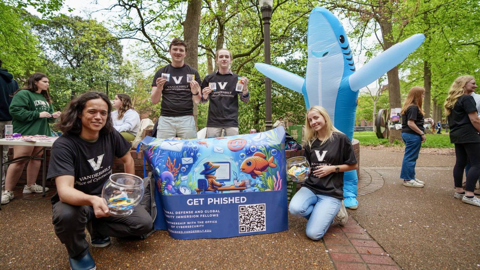 four students outside smiling holding up a "get phised" sign