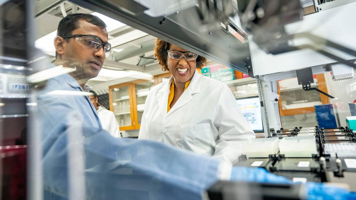 a female professor smiles at a student as they look at chemistry equipment in a laboratory