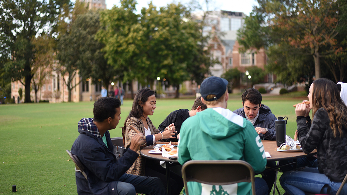 Students eat outside at a table on Alumni Lawn