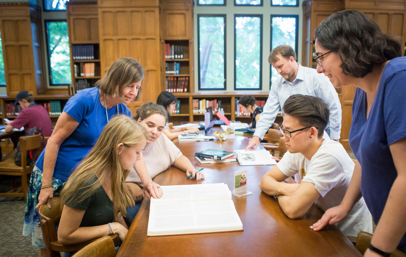 librarians stand behind students seated at a table, smiling
