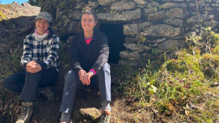 Michelle Young and Natalia Sawyer outside sitting in front of a chullpa, an ancient Andean mausoleum