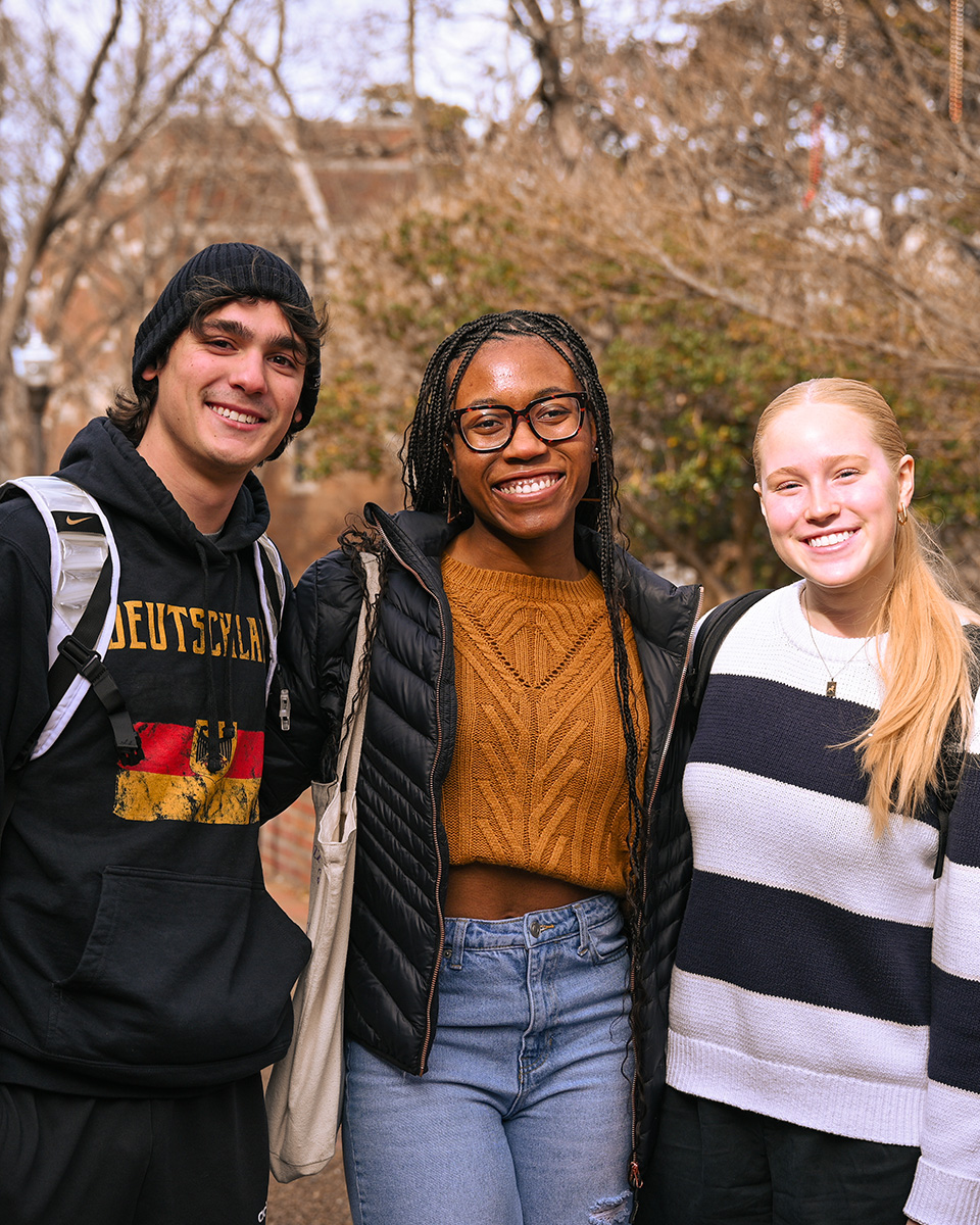 three students smiling stand next to eachother outside