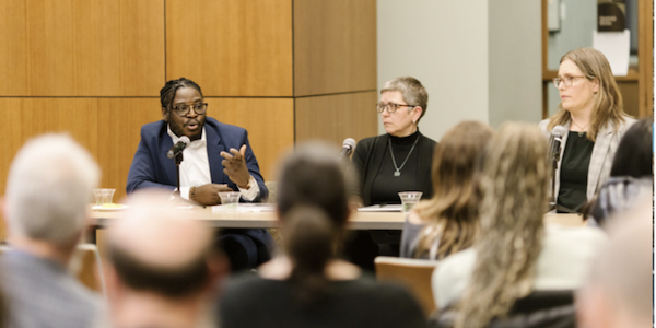 Three people in a panel speaking in front of crowd