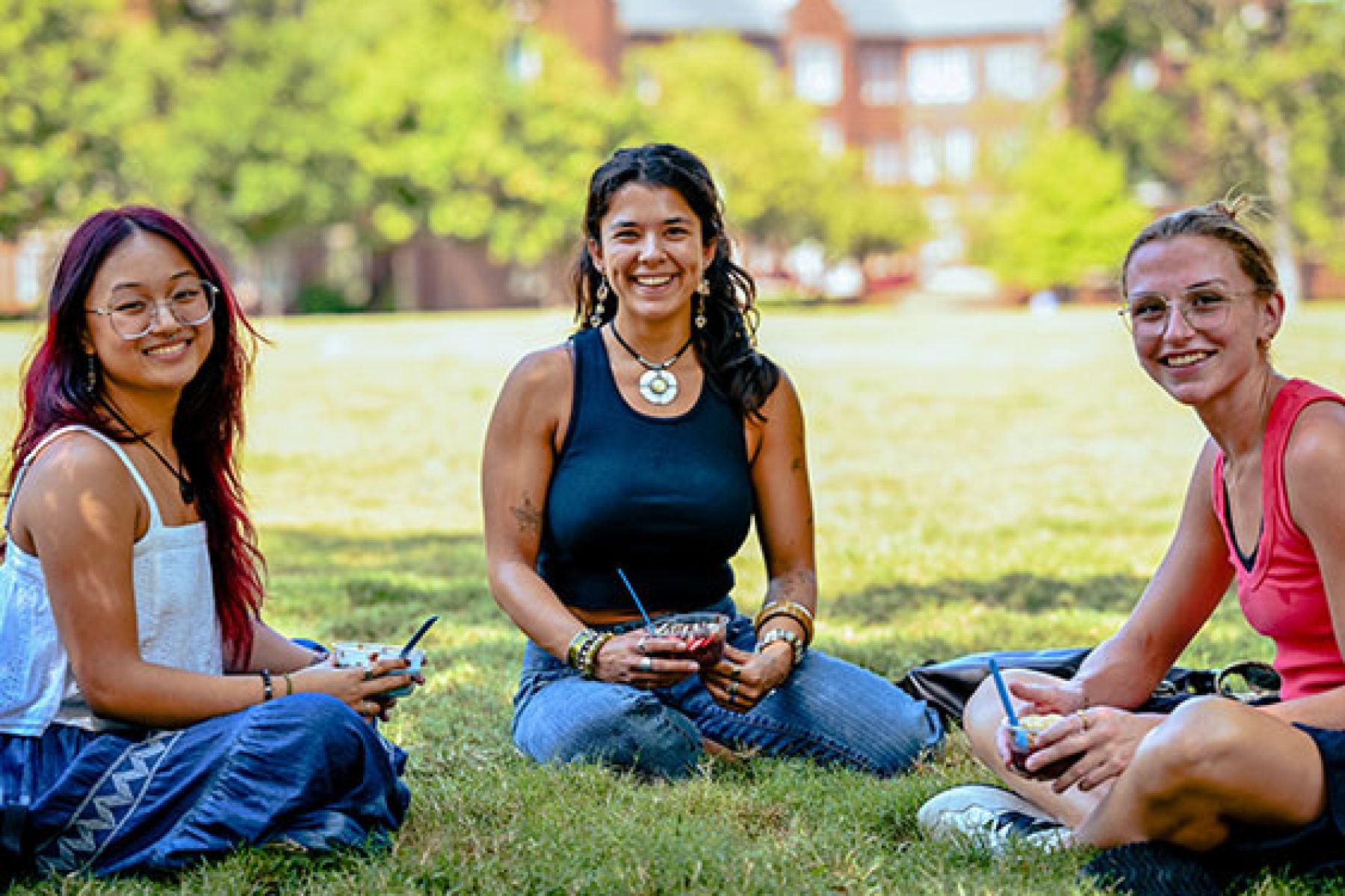Three students sit on the grass outside