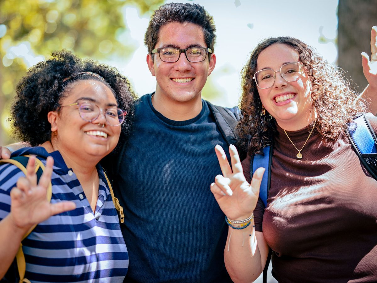 Three students pose for a photo outside with the 