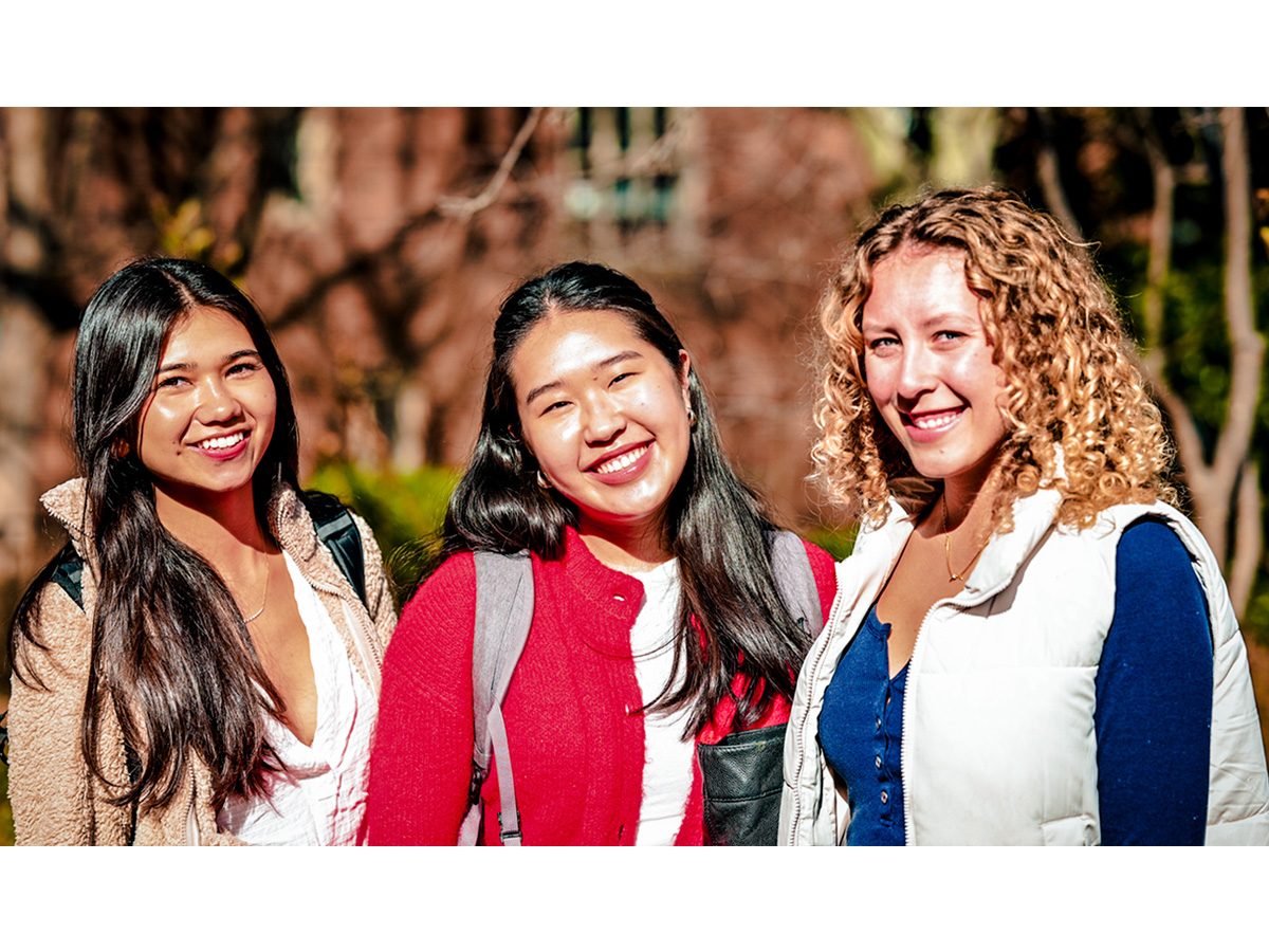 Three female students posing for a photo outside on a sunny day